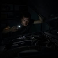 Persona intentando alumbrar el motor de un carro de noche con la linterna del celular