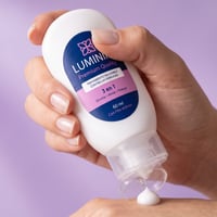 Mano aplicando una gota de la crema Luminiix 3 en 1 desde el frasco original